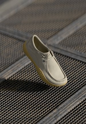 Light gray shoe made of textured material with rubber sole. Features stitching and lacing, elevated heel, and a flexible design for comfort.