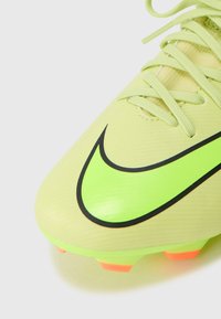 Botín de fútbol amarillo brillante con un gran logo de Nike Swoosh en negro, material texturizado y acentos naranjas en la suela. Cordones visibles.
