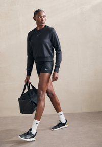 Zwarte sweatshirt met Nike-logo, zwarte shorts met stippenpatroon, zwart en groene schoenen, witte sokken, een zwarte sporttas dragend.
