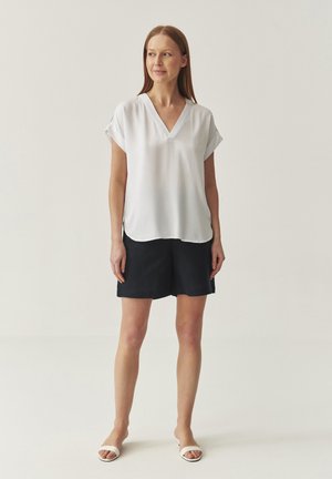 Witte blouse met korte mouwen en een V-hals, gecombineerd met marineblauwe shorts. Gladde textuur, ontspannen pasvorm en afgeronde zoomdetails.