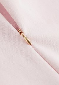 Helles rosa Gewebe mit einem zentralen Reißverschluss und einem goldenen Zugknopf. Die Textur ist glatt mit einem dezenten, atmungsaktiven Webmuster.