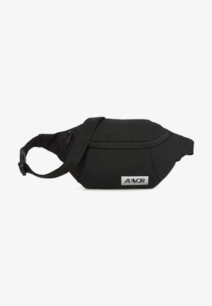 Schwarze Stoff-Gürteltasche mit geschwungener Form, verstellbarem Tragegurt und vorderer Reißverschlusstasche. Enthält ein silbernes Logo-Patch.