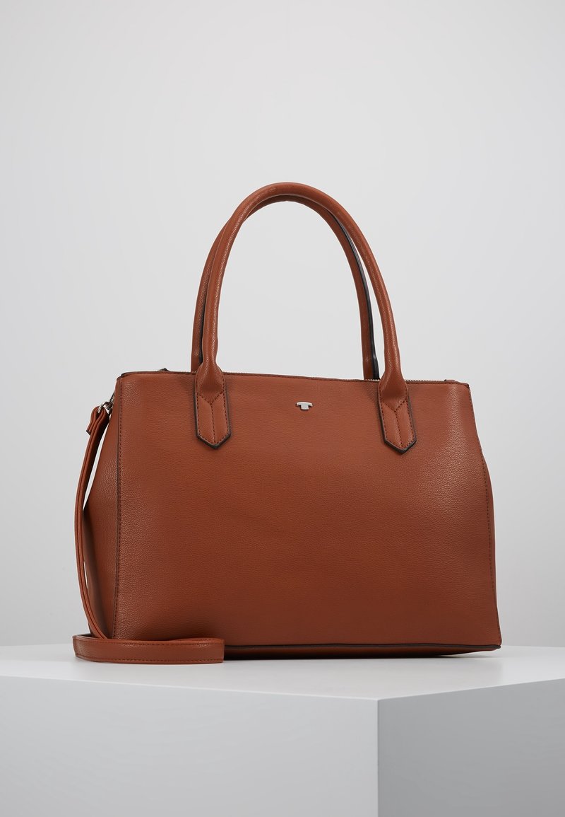 Sac à main en cuir marron avec deux poignées et une bandoulière détachable, posé sur une surface blanche sur un fond gris uni.