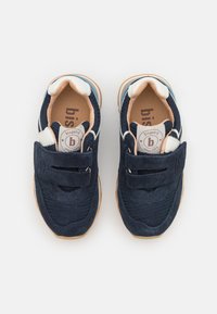 Baskets navy blue pour enfants avec des bandes Velcro, accents blancs, semelles intérieures beiges et semelles couleur marron clair, vues de dessus sur un fond blanc.
