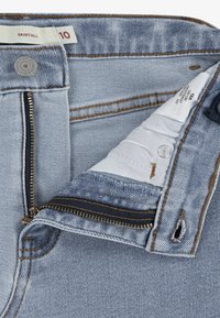 Denim suknja s naramenicama u svijetloplavoj boji s otkrivenim zatvaračem, izblijedjelom teksturom i kontrastnim šavovima. Oznaka pokazuje veličinu 10 i informacije o njezi unutar.