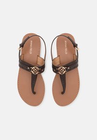 Bruine platte sandalen met een gladde binnenzool, bijpassend bruine voetbed, decoratieve zwarte band met een gouden cirkelaccent en een verstelbare enkelband.