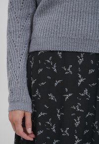 Pulover gri tricotat cu mâneci texturate. Asortat cu o fustă neagră ce are modele florale mici și delicate în nuanțe de albastru deschis și alb.