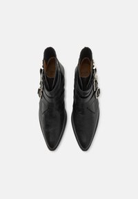 Botine negre din piele, până la gleznă, cu vârf ascuțit, având un design stratificat și trei catarame argintii pe partea exterioară. Detalii texturate prezente.
