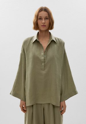 Chemise oversize en lin vert clair, avec un col, trois boutons et des manches larges, portée avec un bas assorti dans un design simple.