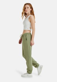 Witte cropped tanktop met uitsnijding, gecombineerd met losse olijfgroene trainingsbroek en witte platform sneakers.