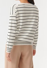 Maglione a righe in crema con righe nere, con colletto a giro e orlo a coste. Il materiale sembra morbido e lavorato a maglia, con una vestibilità comoda.