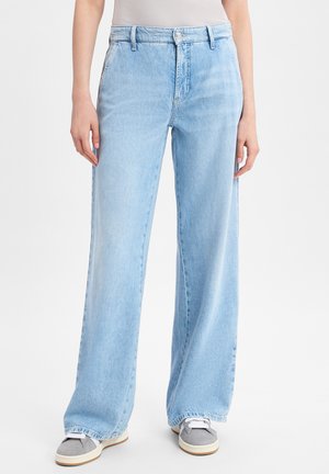 Helles blauweites Jeans mit hoher Taille und subtiler Ausbleichung. Ausgestattet mit Fronttaschen und einem Knopfverschluss. Kombiniert mit grauen Sneakers.