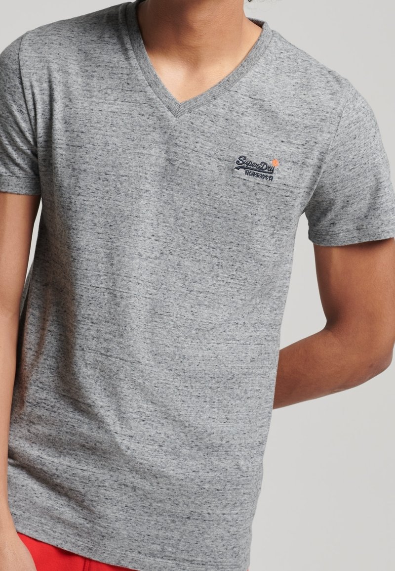 T-shirt grigio a collo a V realizzato in un tessuto morbido e strutturato. Presenta un piccolo logo blu sul petto e maniche corte.