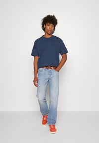 Camiseta de algodón azul marino, de manga corta, combinada con pantalones vaqueros azul claro y zapatillas deportivas naranjas. Un cinturón de cuero marrón añade detalle.