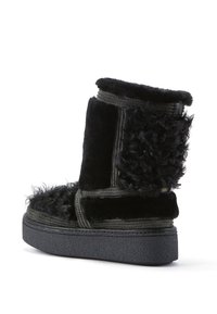 Stivale alla caviglia in pelliccia sintetica nera con accenti testurizzati e soffici. Presenta una suola nera chunky e cuciture rinforzate lungo la parte superiore.