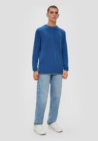 Blaues langärmeliges Strickpullover mit strukturiertem Muster, rundem Halsausschnitt und gerippten Bündchen, kombiniert mit hellblauen geraden Jeans und weißen Sneakers.