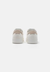 Baskets blanches avec des accents en cuir beige, présentant un dessus texturé, un col rembourré et une semelle en caoutchouc lisse. Vue arrière.