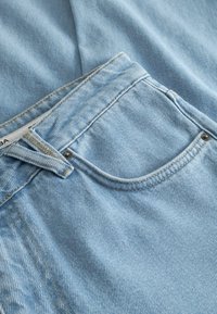 Jeans in denim azzurro chiaro con una tasca frontale e cuciture dorate a contrasto lungo le cuciture. Il materiale presenta un aspetto morbido e strutturato.