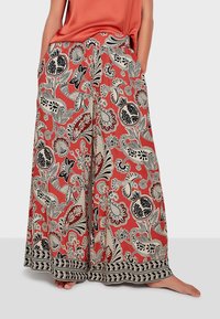 weit geschnittene Hose in Korallenfarbe mit einem schwarz-weißen Blumenmuster. Sie verfügt über einen elastischen Taillenbund und eine dekorative schwarze Bordüre am Saum.