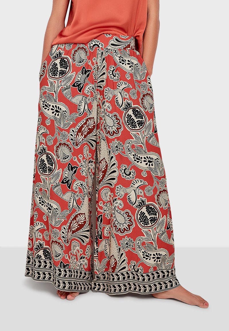 weit geschnittene Hose in Korallenfarbe mit einem schwarz-weißen Blumenmuster. Sie verfügt über einen elastischen Taillenbund und eine dekorative schwarze Bordüre am Saum.
