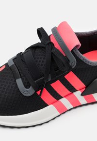 Zapatilla Adidas negra y rosa con parte superior de malla, cordones negros, tres franjas rosas en el lateral y suela blanca con franjas de acento rosas.