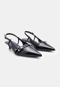 Fekete patent bőrből készült slingback cipők, hegyes orral, elöl két vékony pánttal és ezüst csat díszítéssel. Alacsony sarokkal tervezve.
