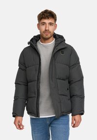 Puchowa czarna kurtka z kapturem, z zapięciem na zamek, bocznymi kieszeniami i małym logo na piersi. Noszona na jasnoszarym swetrze.