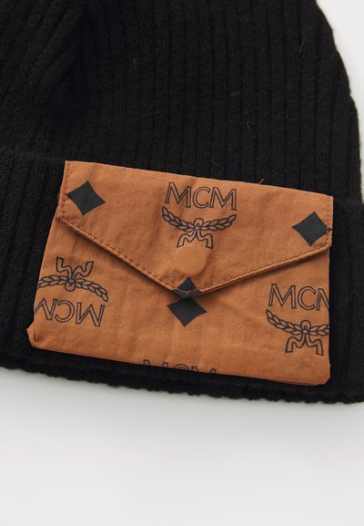Svart rillestrikket lue med en brettet brun konvoluttlomme. Lommen har et mønster av 'MCM'-logoen og svarte detaljer.