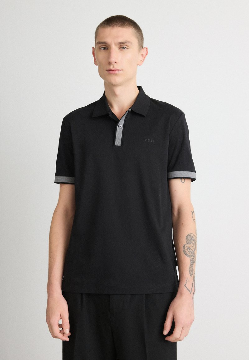 Polo preto com colarinho e detalhes das mangas em cinza. Apresenta um design minimalista e o logótipo 'BOSS' no lado esquerdo. Textura suave.