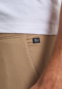 Beige bomuldsbukser har en sidelomme, synlige sømme og et "Petrol Industries" vævsetiket på livet.