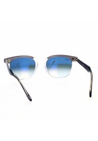 Occhiali da sole con montatura trasparente e lenti blu sfumate. Presentano aste metalliche con un design elegante e dettagli del logo.