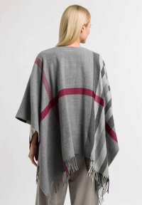 Harmaa ruudullinen poncho, joka on valmistettu pehmeästä materiaalista ja jossa on punaisia ja mustia yksityiskohtia. Siinä on fringed reunat ja löysä, roikkuva muotoilu.