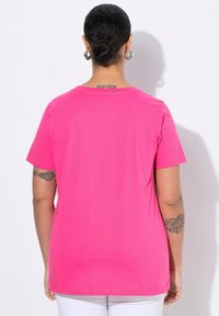 T-shirt à manches courtes, col rond en tissu rose vif. Texture lisse sans motifs. Présente un ourlet droit et de légères coutures sur les côtés.