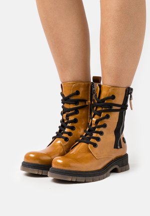 Bottes basses en cuir camel avec lacets noirs, une fermeture éclair latérale et une semelle en caoutchouc grise épaisse. Fini brillant avec des détails texturés.