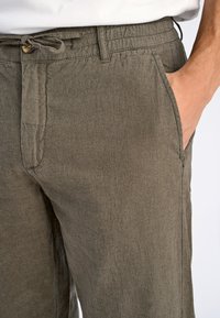 Herrbyxor i olivgrön linne med dragsko i midjan, sidofickor och en texturerad tygyta för komfort och andningsförmåga.