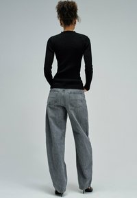 Maglietta nera a coste con maniche lunghe abbinata a jeans in denim grigi a vita alta e dal taglio morbido, con tasche posteriori e una texture sbiadita.