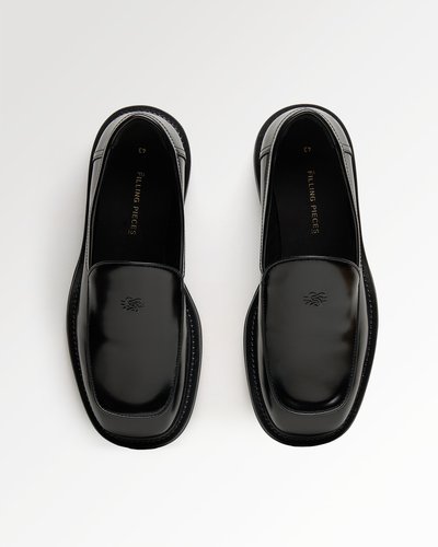 Par crnih koženih slip-on mokasina s kvadratnim vrhovima i suptilnim utisnutim logotipima, prikazani na bijeloj pozadini.