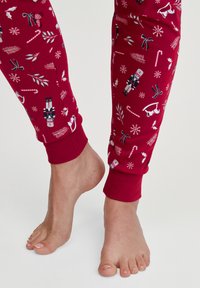 Rode pyjamabroek met een speels vakantiethema van notenkrakers, zuurstokken en sneeuwvlokken. De boorden zijn geribbeld voor een comfortabele pasvorm.