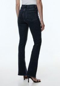 Jeans en denim bleu foncé évasés avec poches arrière et coutures visibles, ajustés au niveau des hanches et une taille mi-haute.