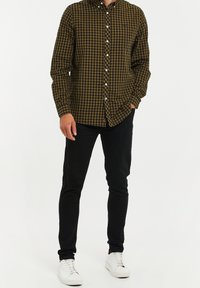Tjekket skjorte i sort og gul, lange ærmer, afslappet pasform, båret med slanke sorte bukser og hvide sneakers.