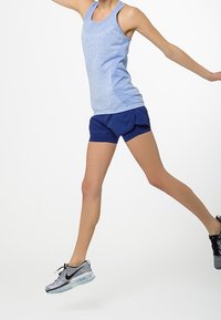 Ljusblå träningslinne och marinblå shorts, med en texturerad tyg, i kombination med gråsvarta sneakers med en genomskinlig sula.