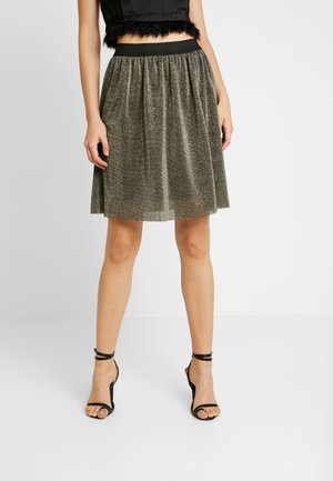 Błyszcząca, metaliczna, ciemnozielona spódniczka typu skater z elastycznym pasem, sięgająca do połowy uda, zestawiona z czarnymi sandałkami na paski.