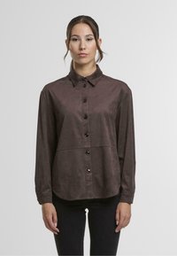 Brown, button-up shirt made of soft, matte fabric. Features a collar, long sleeves, and a curved hem. Black buttons are prominent.