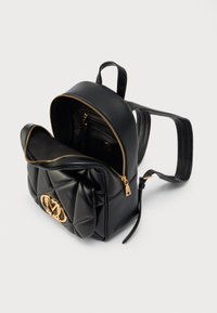 Μαύρο δερμάτινο σακίδιο με ανάγλυφο σχέδιο, χρυσά μεταλλικά στοιχεία και διακοσμητικό λογότυπο. Διαθέτει κλείσιμο με φερμουάρ και εσωτερική τσέπη.