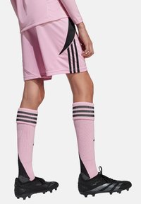 Shorts de sport roses avec des accents noirs, chaussettes hautes rayées noires, et chaussures de football noires avec des détails en argent.