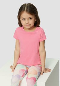Rosa Baumwoll-T-Shirt mit kurzen Ärmeln, das mit drei gestickten Herzen auf der Schulter verziert ist. Kombiniert mit bunten Leggings im Herzen-Design.