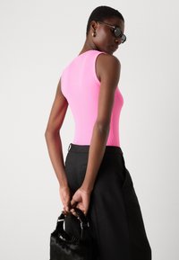 Rosa ribbet bodysuit med ermeløs design, parret med svarte skreddersydde bukser. Modellen holder en liten svart pelsveske med stroppe.