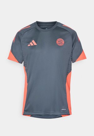 Harmaa urheilu paita oransseilla yksityiskohdilla, jossa on lyhyet hihat, pyöreä kaula-aukko ja FC Bayern Münchenin logo edessä. Valmistettu hengittävästä materiaalista.