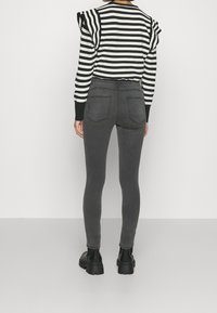 Suéter a rayas en blanco y negro con acentos de hombros con volantes, combinado con jeans oscuros ajustados y botas negras de suela gruesa.