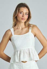 Top bianco senza maniche con scollo quadrato, caratterizzato da ricami floreali e orlo peplum arricciato. Tessuto dalla consistenza liscia.